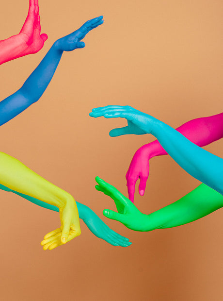 WAVY: This image features five human arms painted in various bright colors. The arms are reaching out towards each other, with the hands in different positions. The background is a simple tan, allowing the vibrant colors of the arms to stand out. This image is a powerful visual representation of connection, communication, and unity.